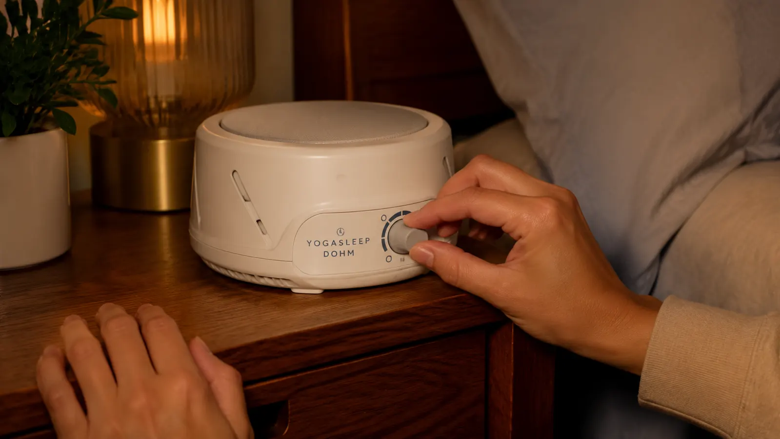 Yogasleep Dohm Classic white noise machine with a hand adjusting the tone dial