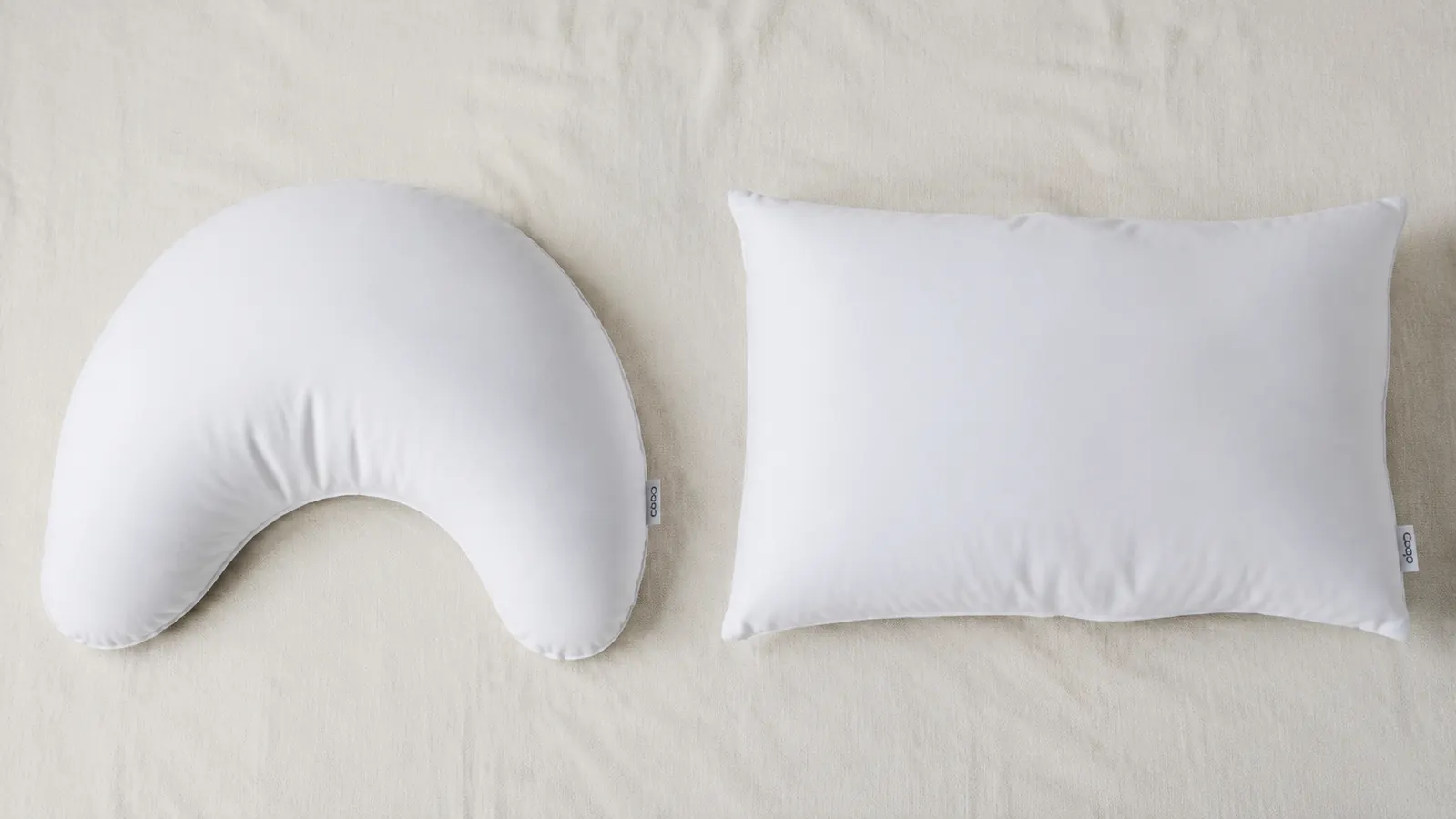 The Coop Crescent pillow sitting next to a traditional rectangular foam pillow, showing the crescent notch on the lower edge