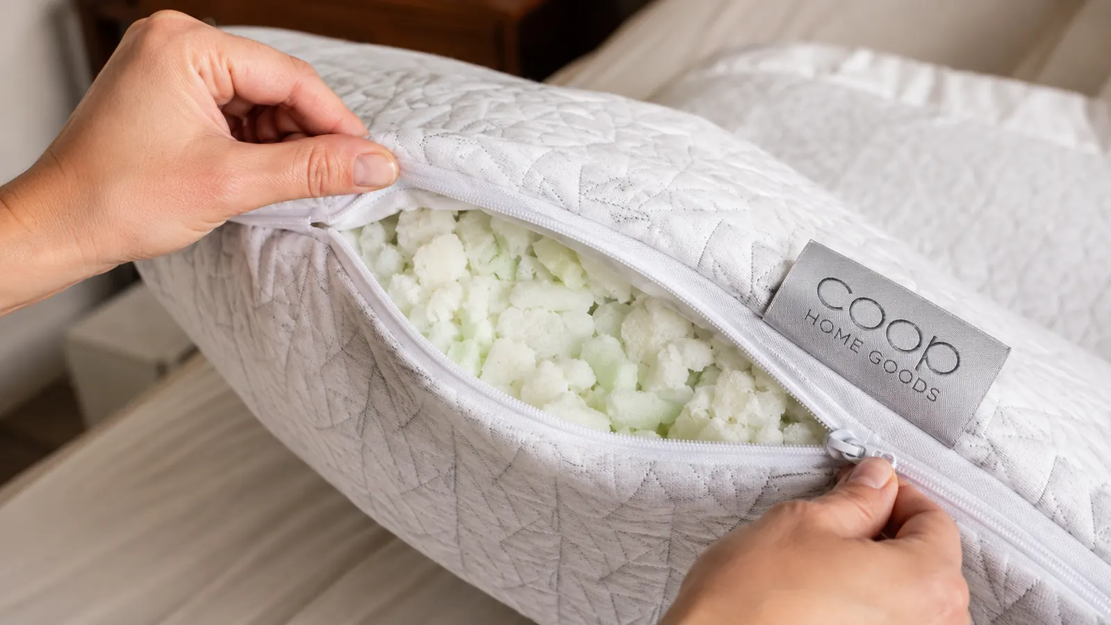 Hands pulling open a zipper on a pillow to adjust the shredded foam fill inside