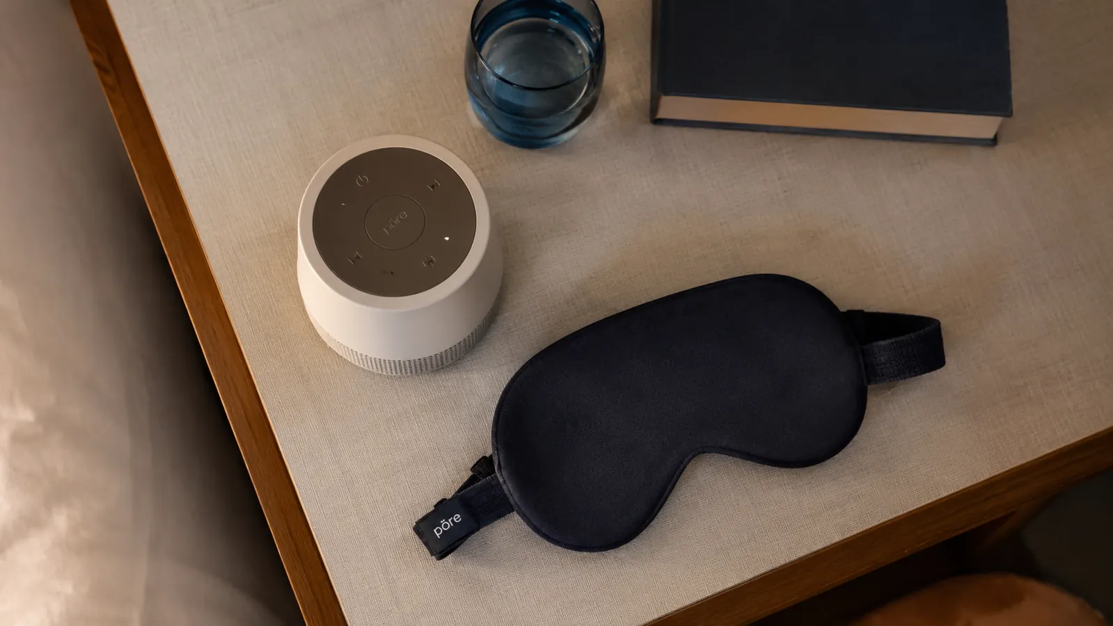 White noise machine paired with a sleep mask on a nightstand, showing a complete sleep setup