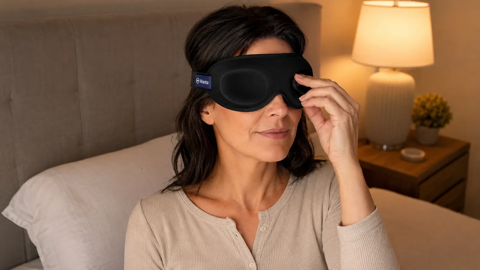 Woman adjusting the Manta sleep mask eye cups before bed, bedside lamp visible in background